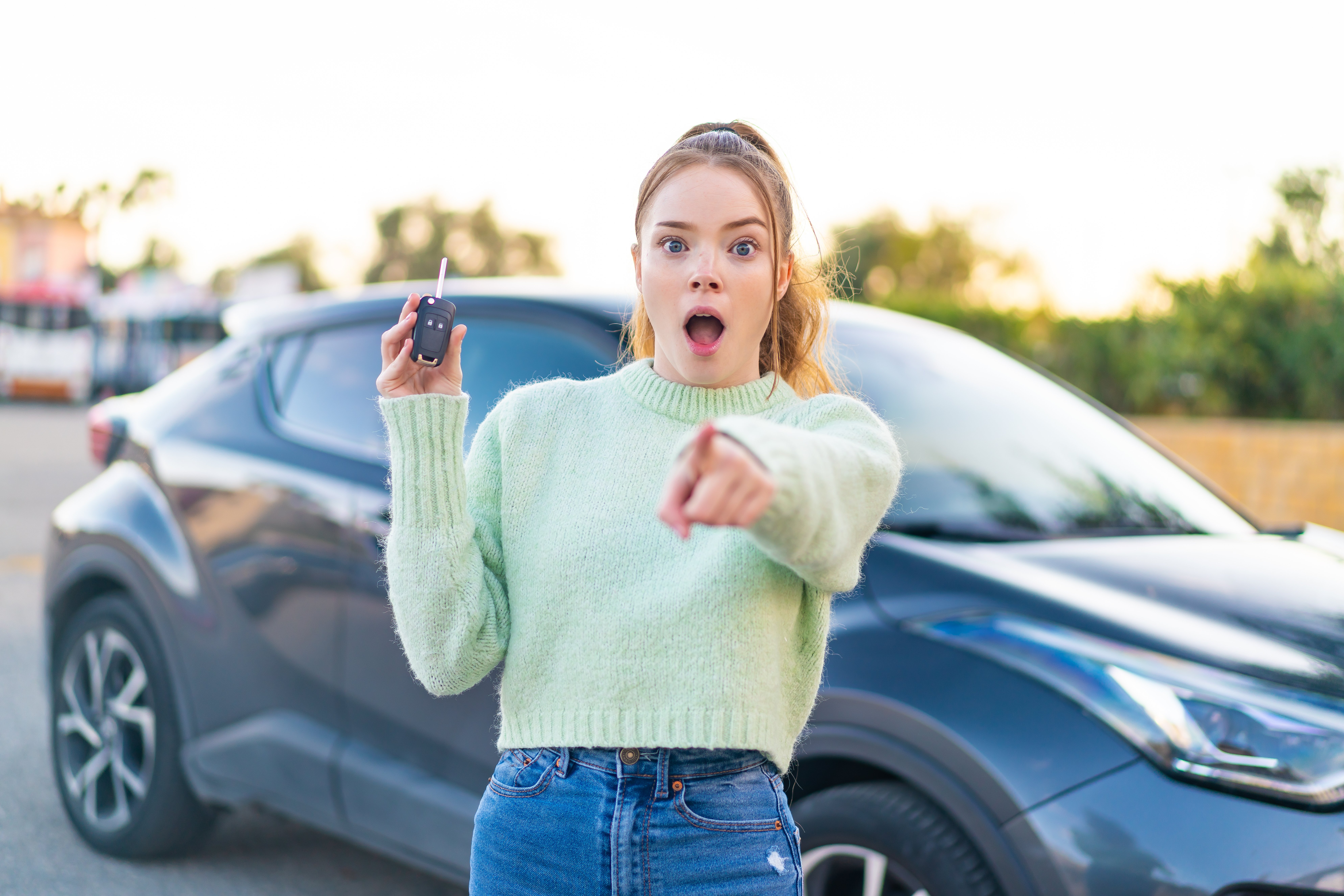 young-pretty-girl-holding-car-keys-outdoors-surprised-pointing-front